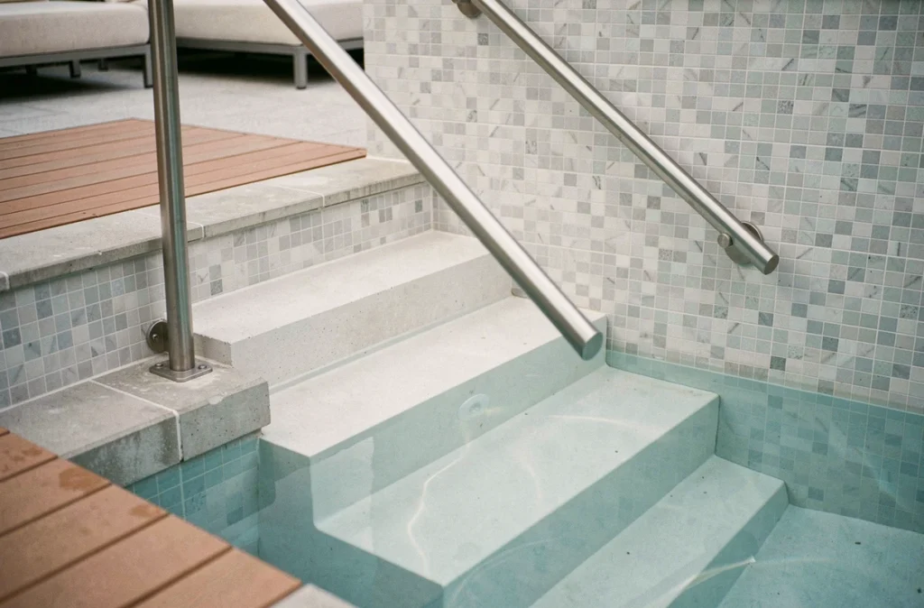 Escalier droit moderne en acier inoxydable dans une piscine contemporaine avec marches en béton blanc immergées